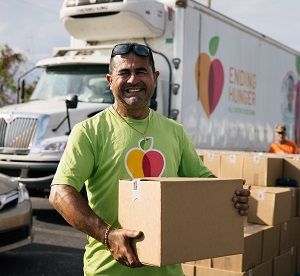 A man smiling while holding a box in front of a delivery truck.