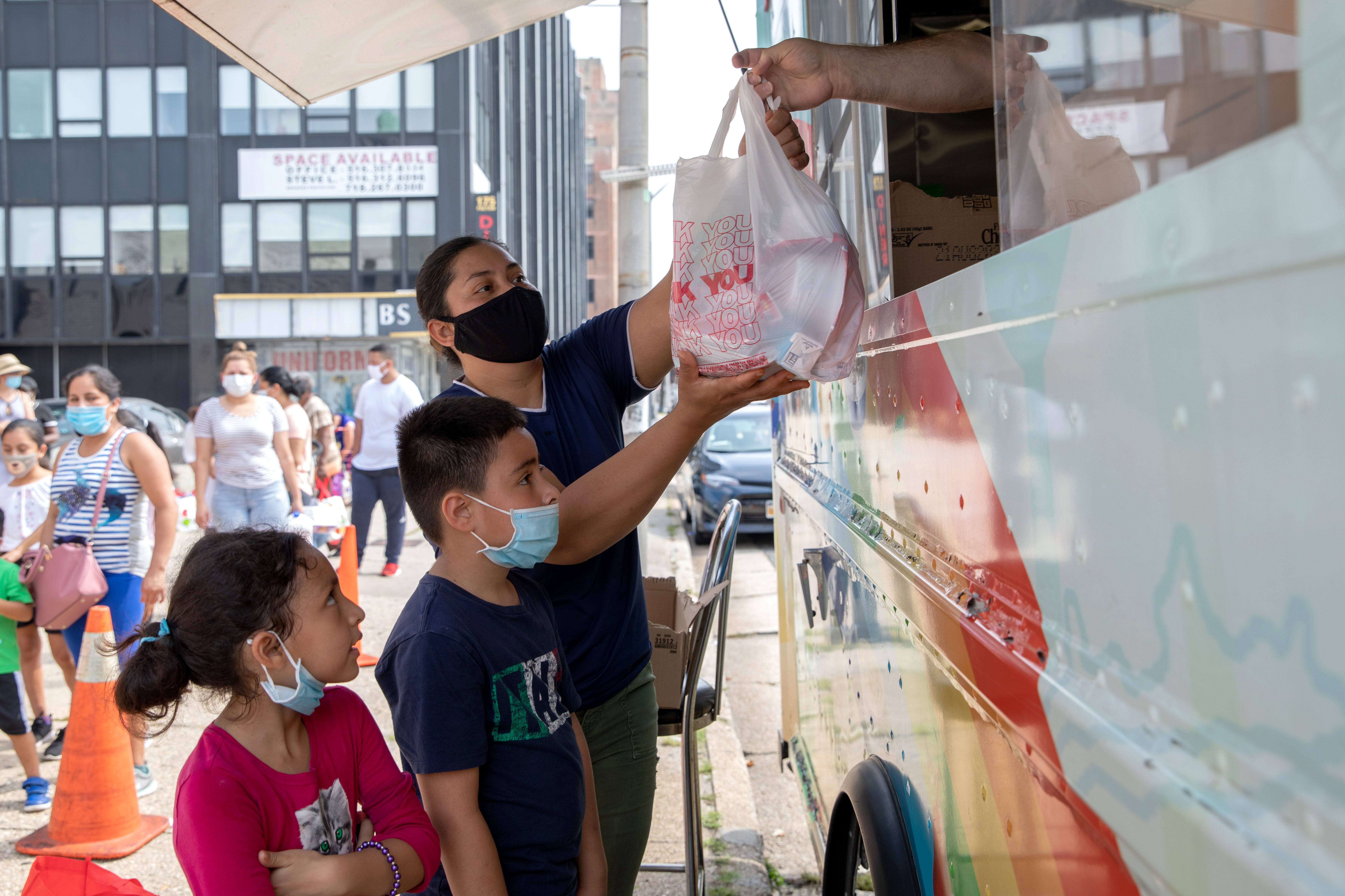 A family receives groceries from a person in a food truck