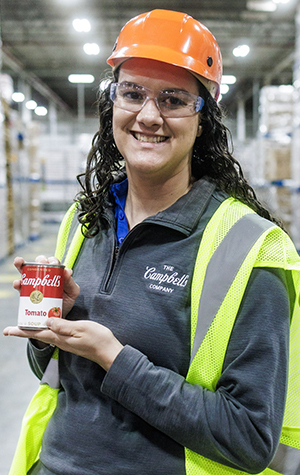 A young person in a warehouse with safety hat and vest