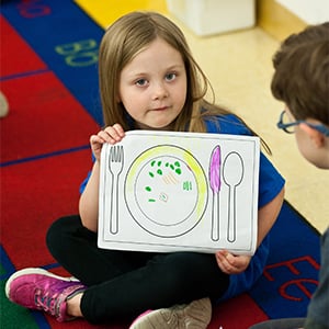 Young girl holding a drawing of a plate.