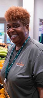 A woman smiles brightly while holding a handful of fresh oranges at a vibrant food distribution.