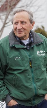 An older man leans against a fence outside a soup kitchen.