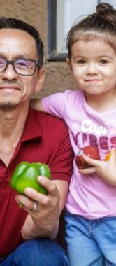 Pedro and his daughter holding fruits and vegetables.