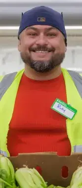 Food bank volunteer holding box of lettuce in front of shelf of produce.