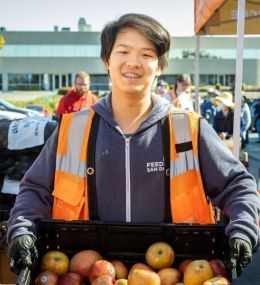 Arthur holding a box of apples, ready to distribute food to his community.