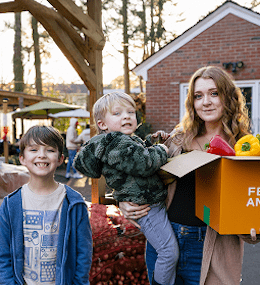 A young woman with two children holds a box of food