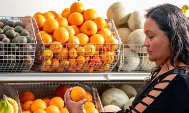 Adriana holding an orange in front of shelves of fruit.