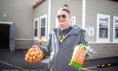 Carl "Hollywood" smiles outside a food distribution site in New York while holding bags of onions and carrots.