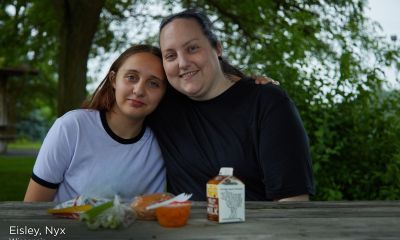Nyx and her daughter Eisley sit together at a picnic table outdoors in Wisconsin, smiling with their arms around each other. Fresh fruit, a carton of milk and other snacks sit on the table in front of them.