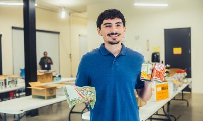 A smiling Angel wearing a blue polo shirt holding various non-perishable food items
