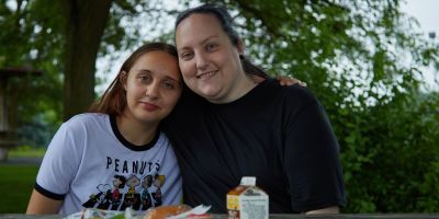 A young woman and her mother lean against each other at a picnic table.