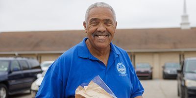 Pastor Dennis carrying a box of food outside of a church.