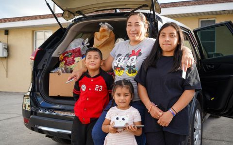 A Latino family standing in front of the opened trunk of their car.