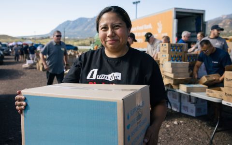 A veteran and volunteer holding a box of food in a food distribution site.
