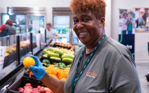 A woman smiles brightly while holding a handful of fresh oranges at a vibrant food distribution.