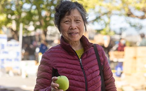 An elderly Asian woman holding a green apple while smiling.