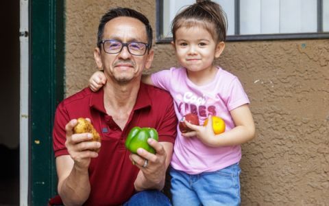Pedro and his daughter holding fruits and vegetables.