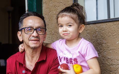 Pedro and his daughter holding fruit and smiling.