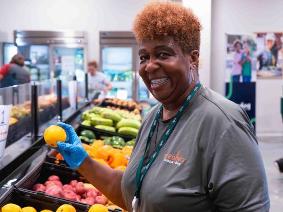  A woman smiles brightly while holding a handful of fresh oranges at a vibrant food distribution.