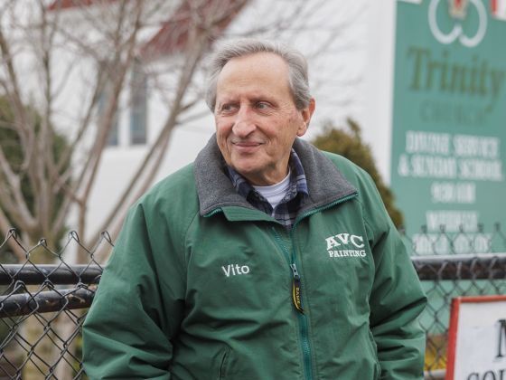 An older man leans against a fence outside a soup kitchen
