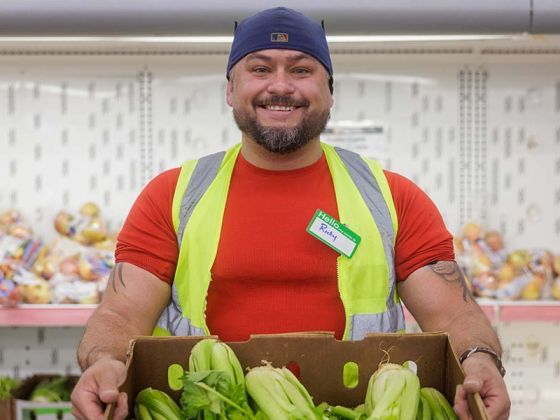 A smiling food pantry volunteer holds a box of fresh celery.