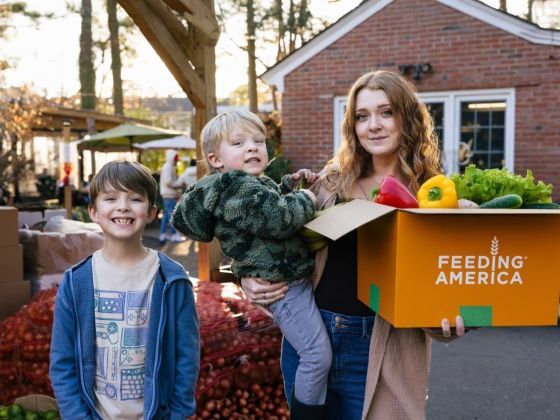 Taylor and her 3 boys outside her home with a box of produce