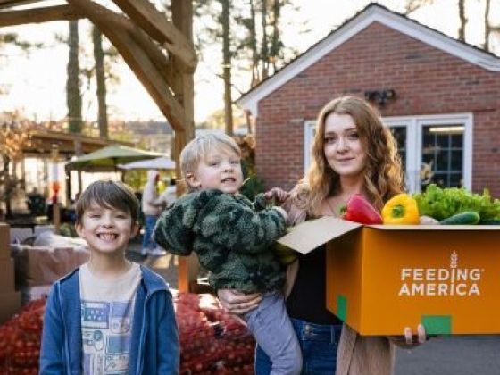 Taylor and her 2 boys outside her home with a box of produce.