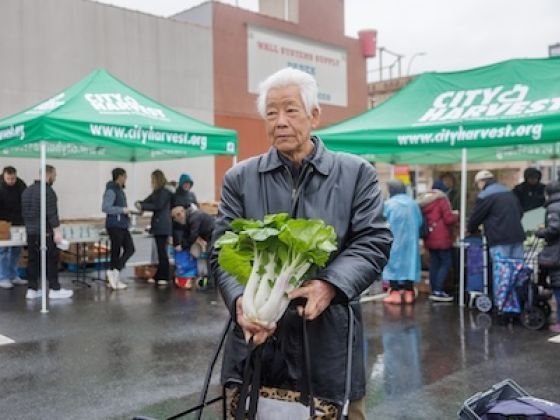 An elderly man holding fresh greens outside of a food pantry