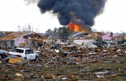 A destroyed house with a fire raging in the background