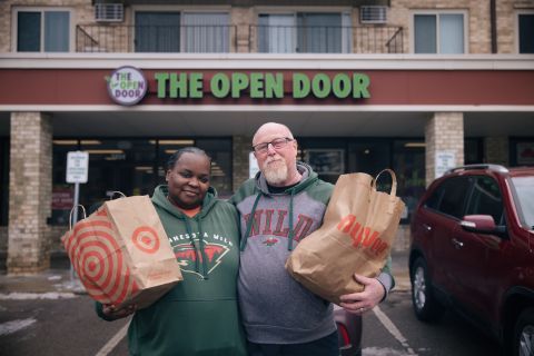 a couple holding paper grocery bags stand in front of The Open Door Pantry