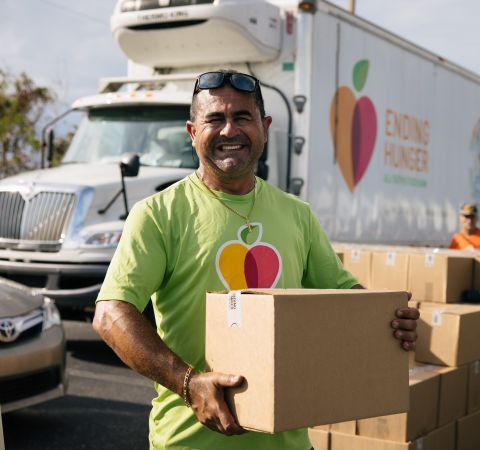 A truck driver holding a box of food in front of a truck.