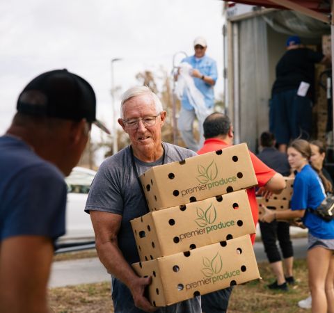 A man holding boxes and helping other volunteers distribute food.