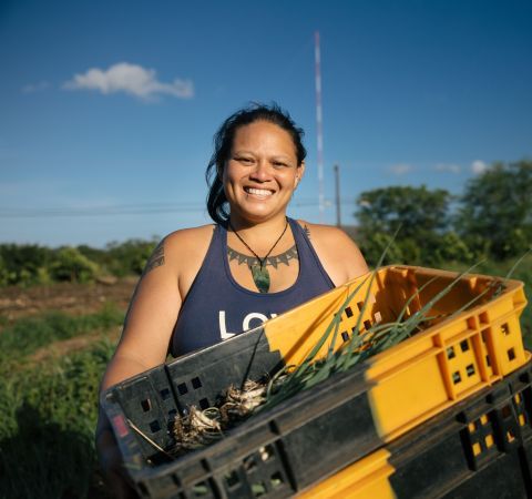 A farmer in a field holding a crate and smiling.