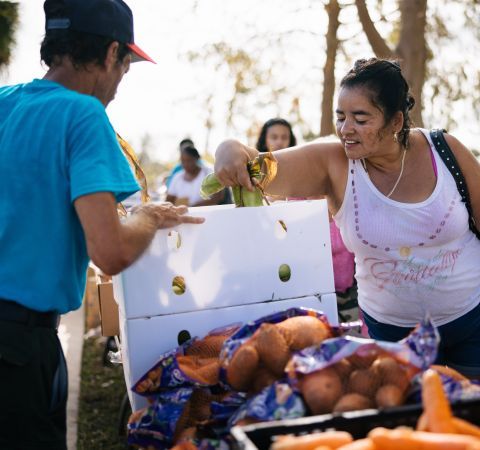 A woman grabbing vegetables while a volunteer assists.