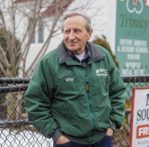 An older man leans against a fence outside a soup kitchen.