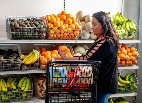 Adriana holding an orange next to a shopping cart.