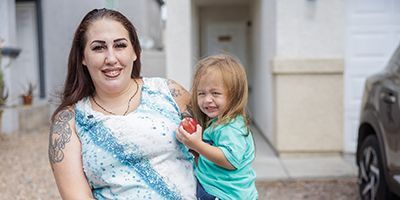 Jessica and her child standing outside of their home.