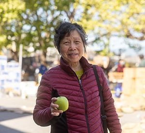 An elderly Asian woman holding a green apple while smiling.