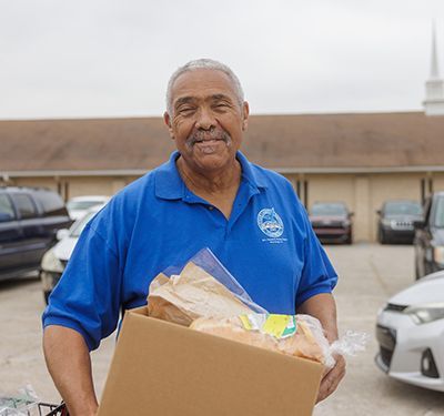 Pastor Dennis carrying a box of food outside of a church.