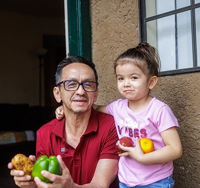 Pedro and his daughter holding fruits and vegetables.