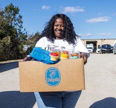 Valerie holding a box of food with cars lined up behind her.