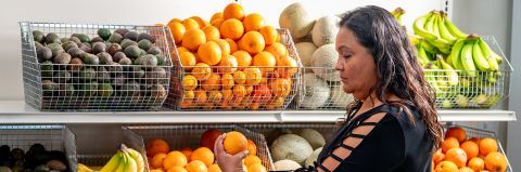 Adriana holding an orange in front of shelves of fruit.