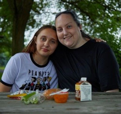 A young woman and her mother lean against each other at a picnic table.