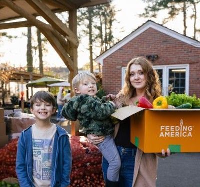Taylor and her 2 boys outside her home with a box of produce.
