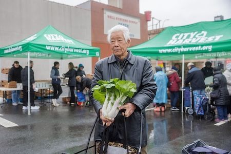 An elderly man holding fresh greens outside of a food pantry