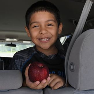 Boy in back seat of car holding apple and smiling