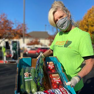 A volunteer at a Mobile Pantry hosted by Northwest Arkansas Food Bank holding a box of produce.