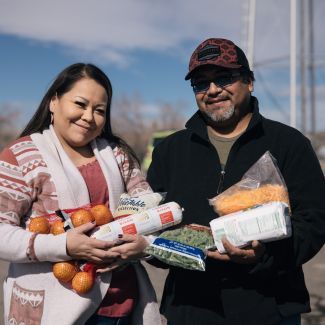 A couple of Native American descent holding food while standing outside.