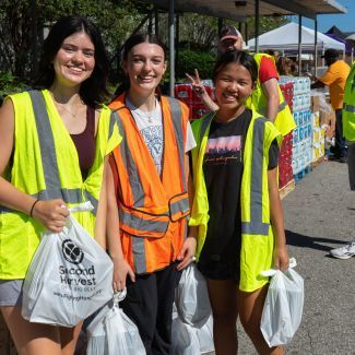 Volunteers wearing high visibility safety vests and holding bags of food.