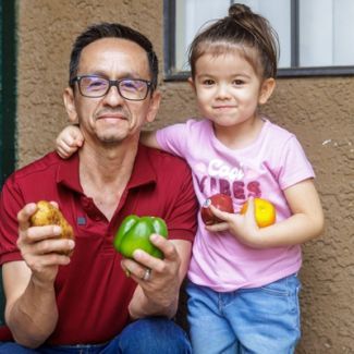 Pedro and his daughter holding fruits and vegetables.